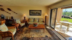 A cozy living room with a sofa, chairs, a coffee table, and a dining area. There is a large window with a view of greenery outside. - "Front Row"  Ocean & Island Views 2 Bedroom (Maunaloa)