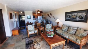 A living room with a sofa, chairs, a coffee table, and a dining table. There is a kitchen in the background. - "Front Row"  Ocean & Island Views 2 Bedroom (Maunaloa)