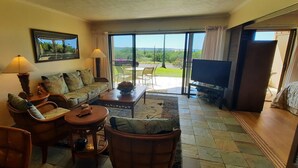 A spacious living area with a sofa, chairs, a coffee table, and a television. There is a large window offering a view of the outdoors. - "Front Row"  Ocean & Island Views 2 Bedroom (Maunaloa)