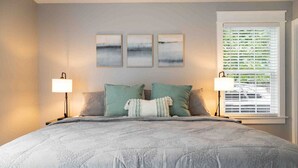A bedroom with a large bed, two bedside lamps, three wall-mounted paintings, and a window with blinds. - Bearden Exec · Bearden Executive Rental >8min to UT & Downtown (Knoxville)