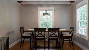 A dining area with a wooden table and chairs, a chandelier, and a window with blinds. - Bearden Exec · Bearden Executive Rental >8min to UT & Downtown (Knoxville)