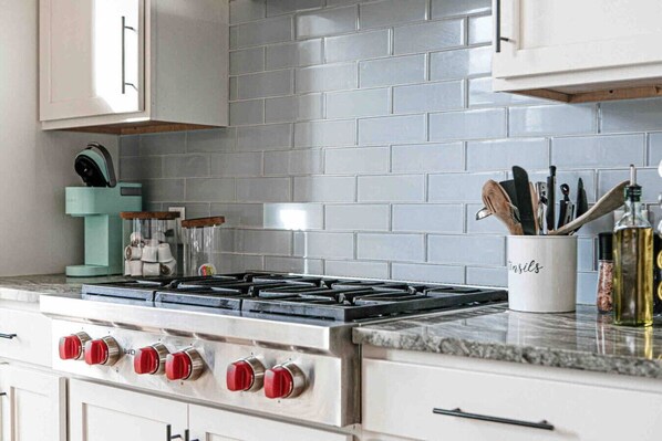 A kitchen with a gas stove, white cabinets, and a tiled backsplash.