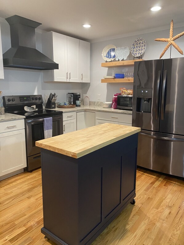 A modern kitchen with white cabinets, a black range hood, a stainless steel refrigerator, and a wooden island.