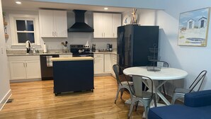 A compact kitchen with white cabinets, a black range hood, and a central island. - Boro Bungalow in beautiful downtown Swansboro with street legal golf cart (Swansboro)