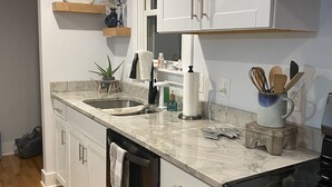A modern kitchen with white cabinets, a marble countertop, and wooden flooring. - Boro Bungalow in beautiful downtown Swansboro with street legal golf cart (Swansboro)