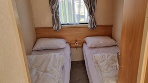 Una habitación pequeña y acogedora con dos camas individuales, una ventana con cortinas y un cabecero de madera.