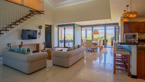 A spacious living area with a high ceiling, a staircase, a dining area, and a kitchen.