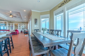 Enjoy family gatherings in this dining area with a long table, high ceiling, and large windows offering a view of the outdoors.