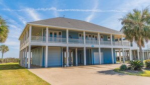 A two-story building with a balcony on the upper floor, a covered parking area, and palm trees in the foreground. - Beautiful Beachfront -- Biscayne Fantasea (Bolivar Peninsula)