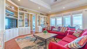 A spacious living room with a red sofa set, a television, and built-in shelving with decorative items. - Beautiful Beachfront -- Biscayne Fantasea (Bolivar Peninsula)