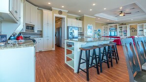 A spacious kitchen with white cabinetry, a central island with stools, and a red accent wall. - Beautiful Beachfront -- Biscayne Fantasea (Bolivar Peninsula)