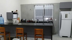 Cocina compacta con una isla central, un refrigerador y un comedor con sillas.
