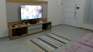Una sala de estar con una televisión de pantalla plana montada en un estante de madera, un tapete a rayas en el suelo y una puerta cerrada al fondo.