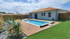 Un patio trasero con piscina, terraza de madera y césped artificial.