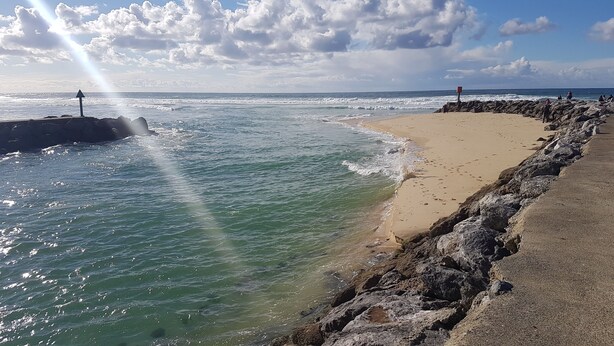 Una playa con costa rocosa, olas y cielo despejado.