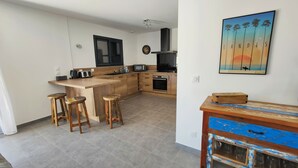 Una cocina moderna con una isla de madera, dos taburetes, un horno empotrado y un cuadro de un atardecer.