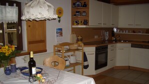 Uma cozinha com armários brancos, uma mesa de jantar de madeira com toalha branca e um vaso de flores amarelas.
