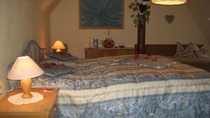 Quarto com cama coberta por roupa de cama estampada, mesa de cabeceira com luminária, quadro na parede e planta decorativa.