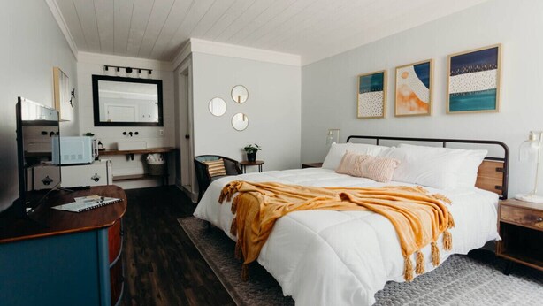 Un dormitorio con cama, mesitas de noche, escritorio, silla, cómoda y televisor.