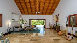 A spacious living room with a high ceiling, a large window, and a view of greenery outside. - Luxurious Casa de Campo Villa for up to 12 people (La Romana)