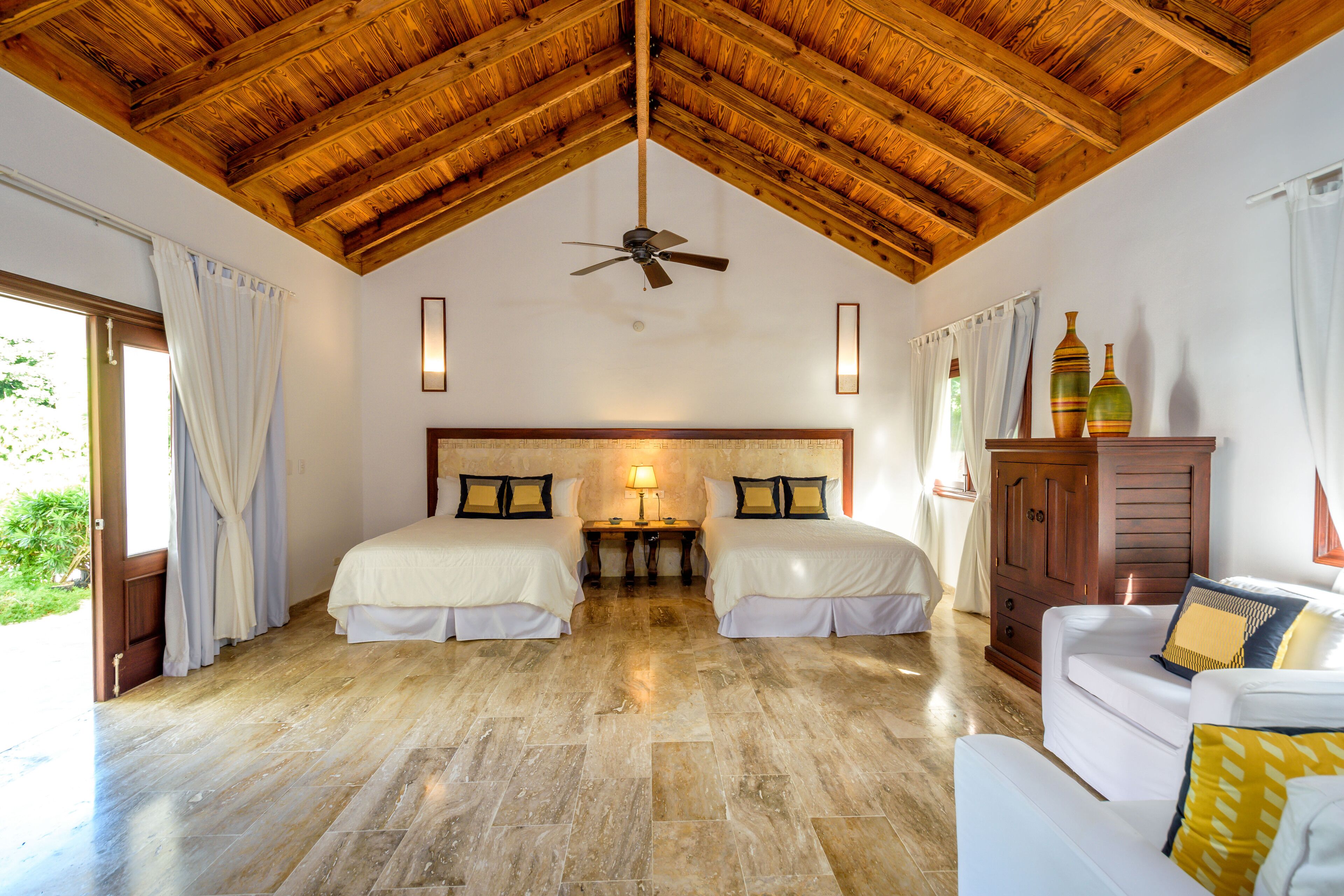 A room with two beds, a ceiling fan, a wooden cabinet, and a couch.