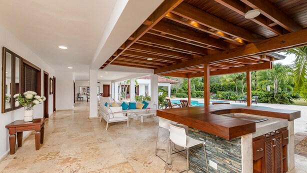 A modern kitchen with a stone island, wooden ceiling beams, and a view of a pool. - Luxurious Casa de Campo Villa for up to 12 people (La Romana)