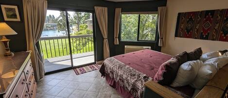 Ein Schlafzimmer mit einem großen Bett, einem Schminktisch, einem Fenster mit Vorhängen und Blick auf einen Balkon.