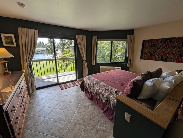 A bedroom with a large bed, a dresser, a window with curtains, and a view of a balcony. - Bay View Luxury Studio (Bigfork)