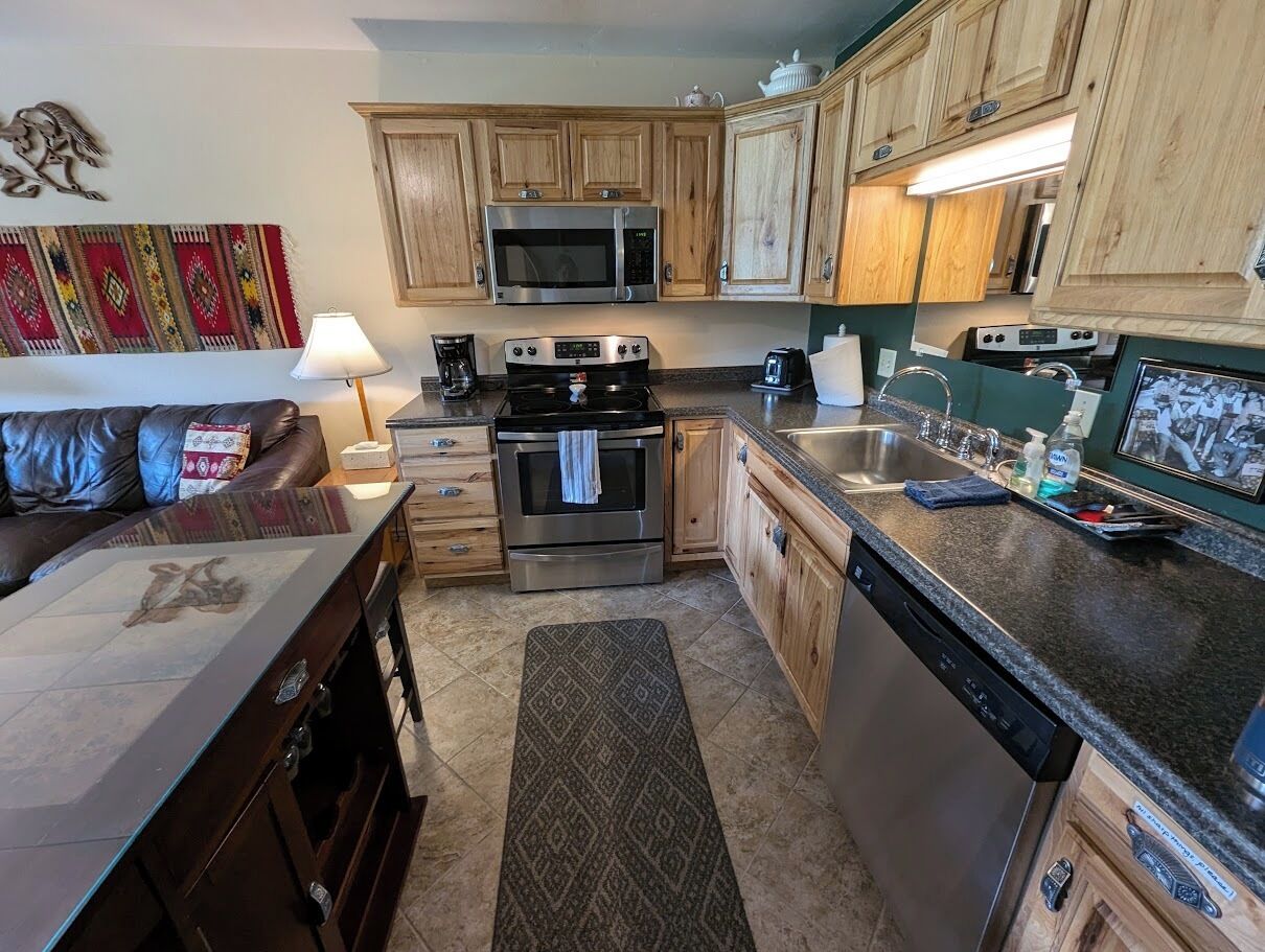A compact kitchen with wooden cabinets, a microwave, a stove, and a dishwasher.