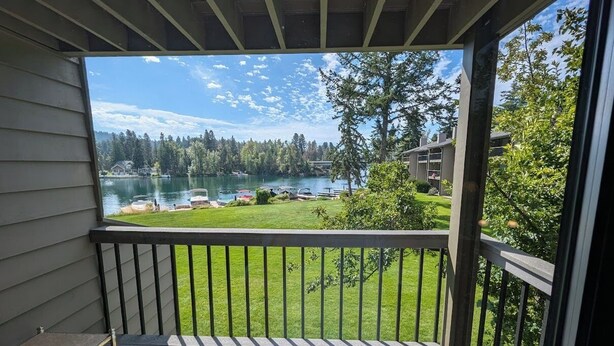 Un balcon donnant sur un lac, une zone herbeuse et un parking avec des voitures.