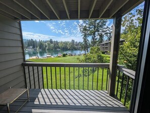 A balcony with a view of a lake, a grassy area, and a parking lot with cars. - Bay View Luxury Studio (Bigfork)