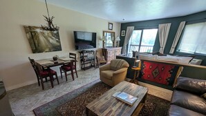Un salon comprenant un téléviseur, un canapé, une table basse et un coin repas avec des chaises et une table.