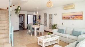 A modern living room with a white sofa, a glass coffee table, and a dining area with chairs and a table. - CALERO DREAM by Buenavilla | 3 bedroom  Frontline villa (Puerto Calero)