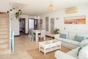 A modern living room with a white sofa, a glass coffee table, and a dining area with chairs and a table.