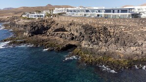 A coastal hotel with multiple floors, a rocky shoreline, and clear blue waters. - CALERO DREAM by Buenavilla | 3 bedroom  Frontline villa (Puerto Calero)