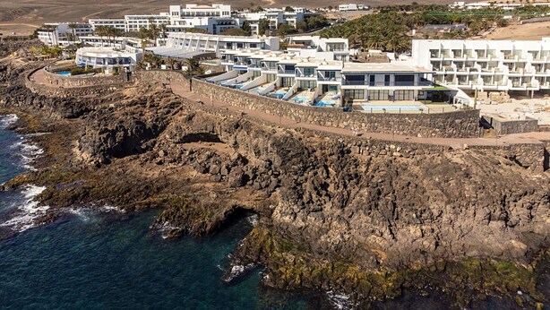 A coastal resort with modern architecture, featuring multiple buildings with balconies, a swimming pool area, and rocky terrain adjacent to the sea. - CALERO DREAM by Buenavilla | 3 bedroom  Frontline villa (Puerto Calero)