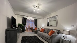 Ein modernes Wohnzimmer mit grauem Sofa, schwarzem Teppich und einem Essbereich im Hintergrund.