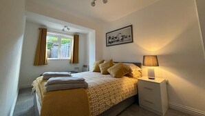 Ein Schlafzimmer mit einem Bett, einem Nachttisch mit Lampe, einem Fenster mit Vorhängen, einem Deckenventilator und einem gerahmten Bild an der Wand.