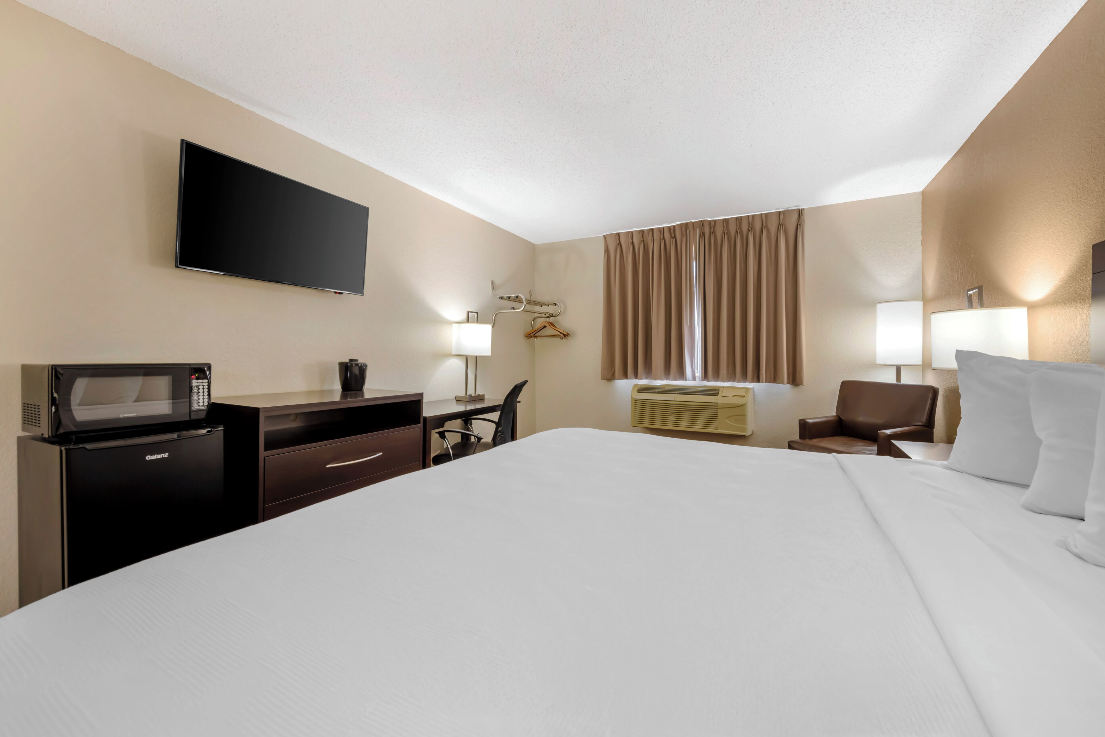 A hotel room with a large bed, a flat-screen TV, a microwave, a desk with a chair, and two bedside lamps.