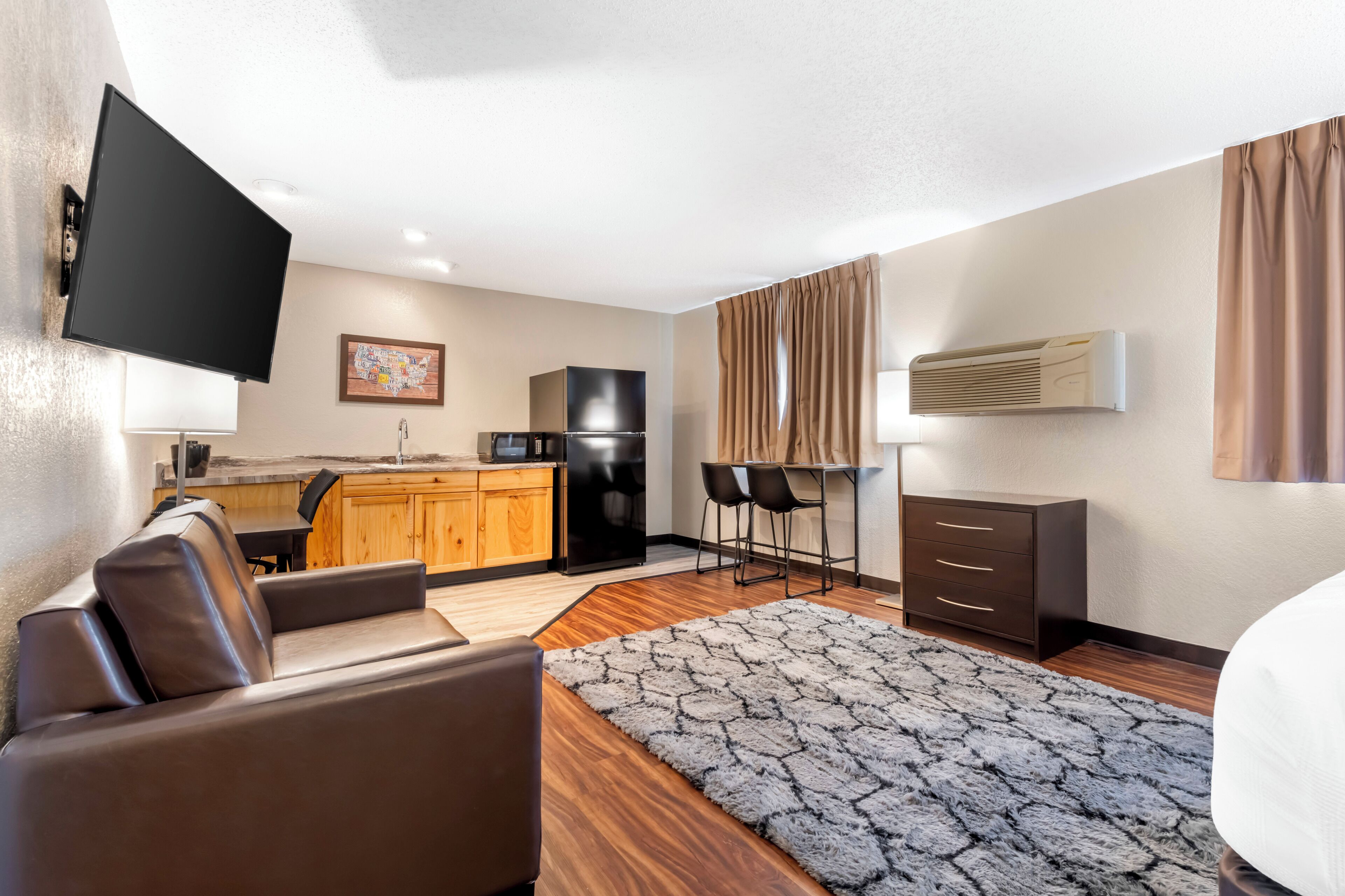 A modern hotel room with a sofa, a TV, a kitchen area with a refrigerator, a bar area, and a bed.