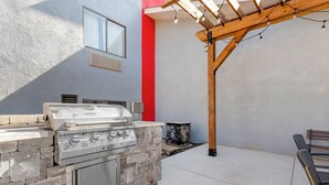 An outdoor kitchen with a built-in grill and oven, a pergola with string lights, and a red wall.