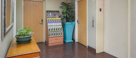 A hallway with a wooden bench, a potted plant, a bulletin board, and a large blue planter.