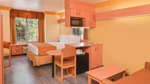 Une chambre d’hôtel de taille réduite, comprenant un lit, une petite kitchenette, un coin repas et une fenêtre avec des rideaux.