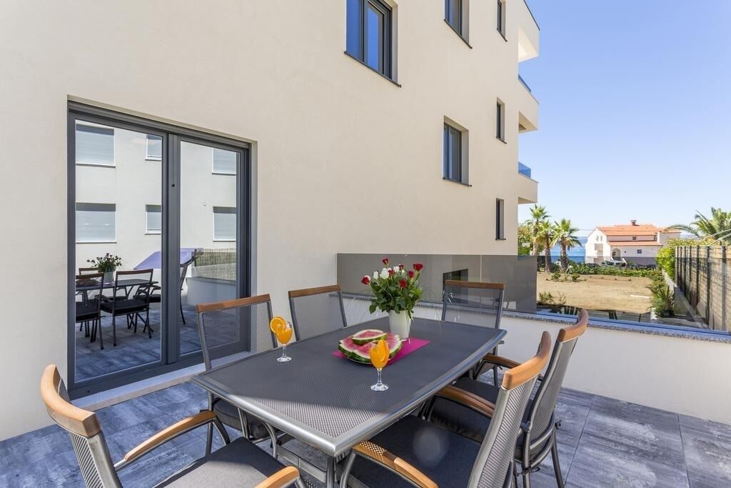 A modern outdoor dining area with a table and chairs, a potted plant, and a view of the surrounding area.