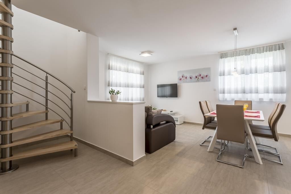 Una sala de estar moderna con una escalera, un comedor con mesa y sillas, y un televisor de pantalla plana en la pared.