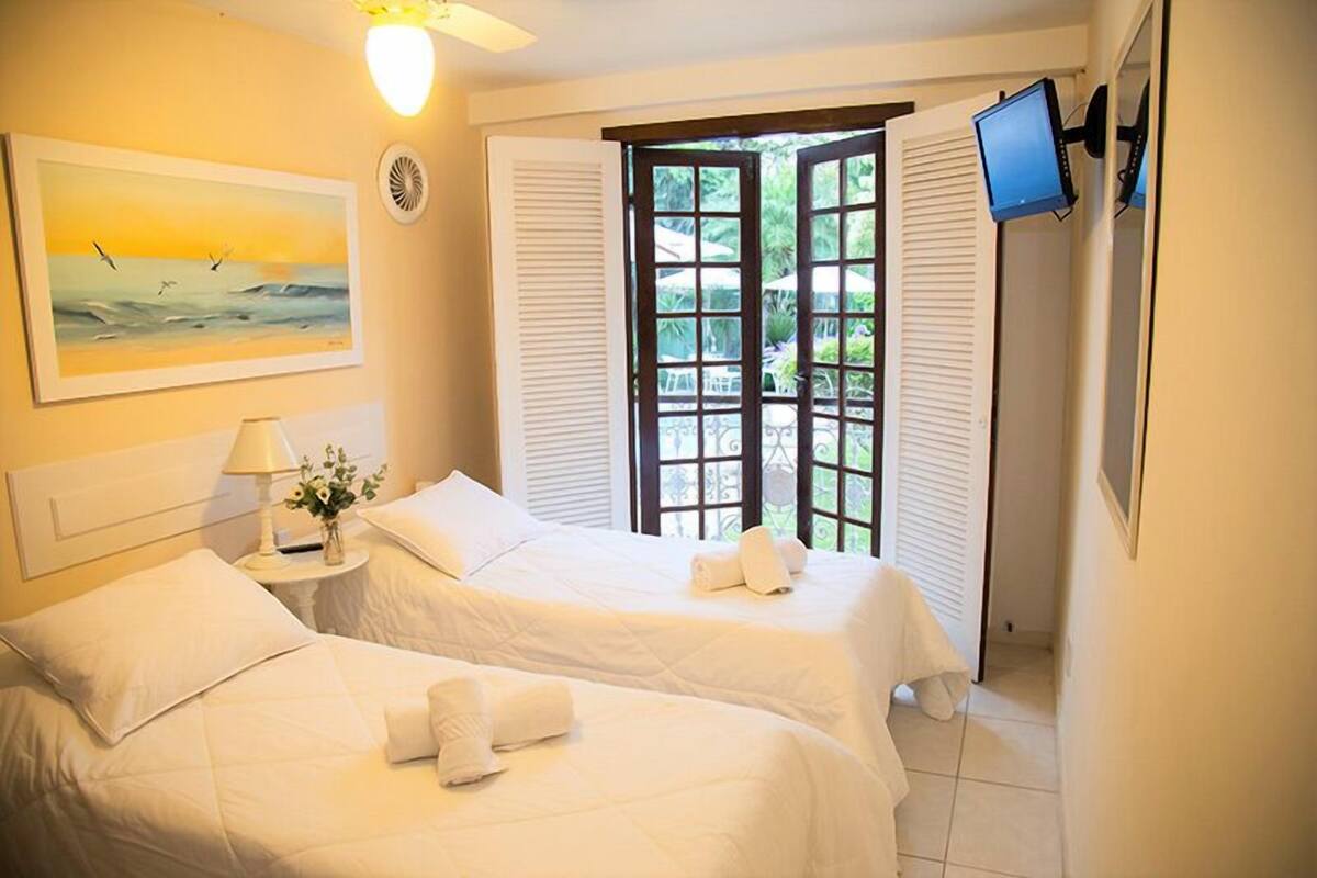 Ein Hotelzimmer mit zwei Betten, einem Gemälde, einem Fernseher und einem Fenster mit Rollläden.