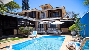 Uma casa de dois andares com piscina, móveis de exterior e um espaço de varanda.