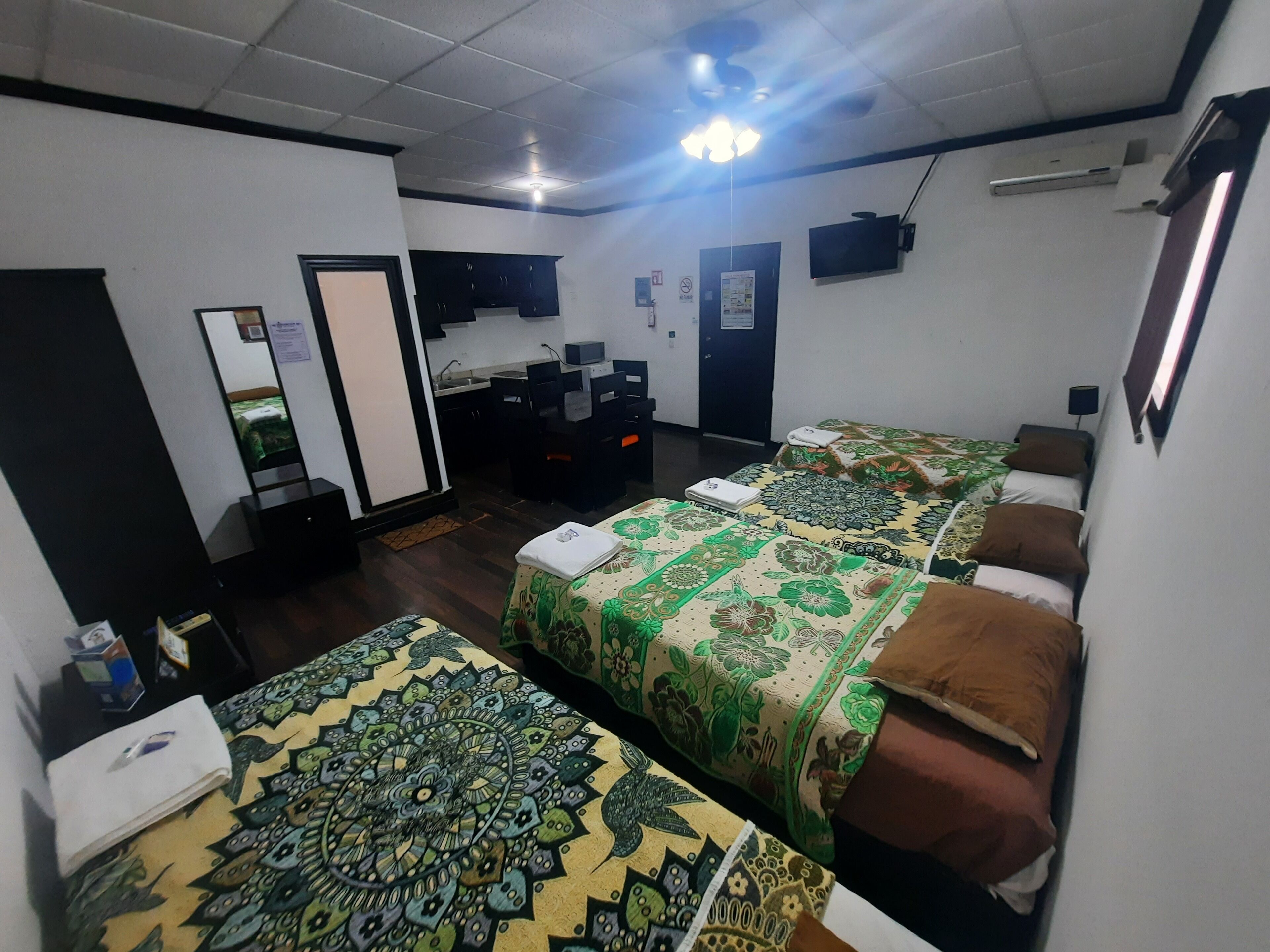 A hotel room with two single beds, a desk with a chair, a wardrobe, a mirror, and a television on the wall.