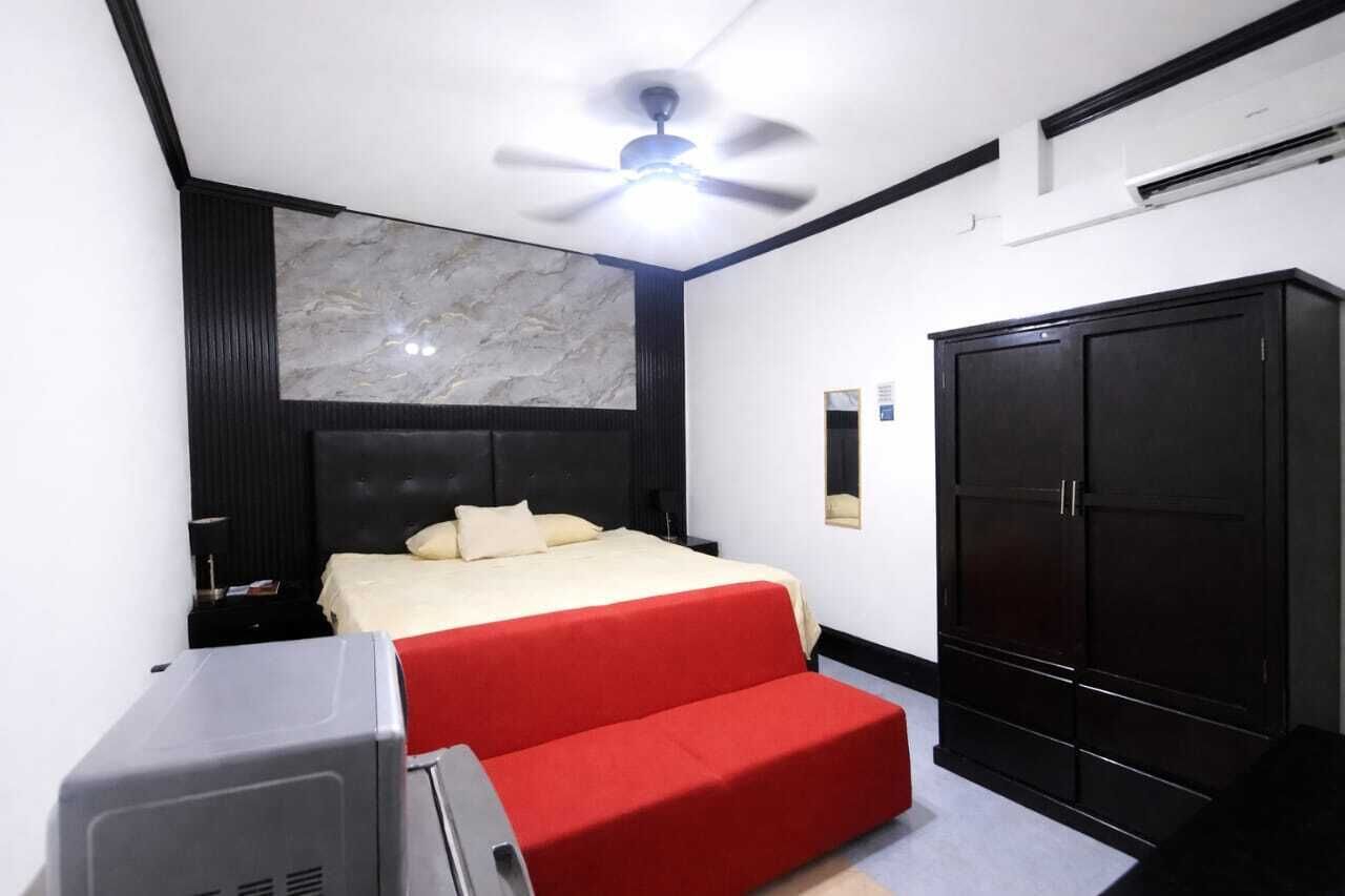 A bedroom with a bed, a red sofa, a ceiling fan, a wardrobe, and a desk with a printer.