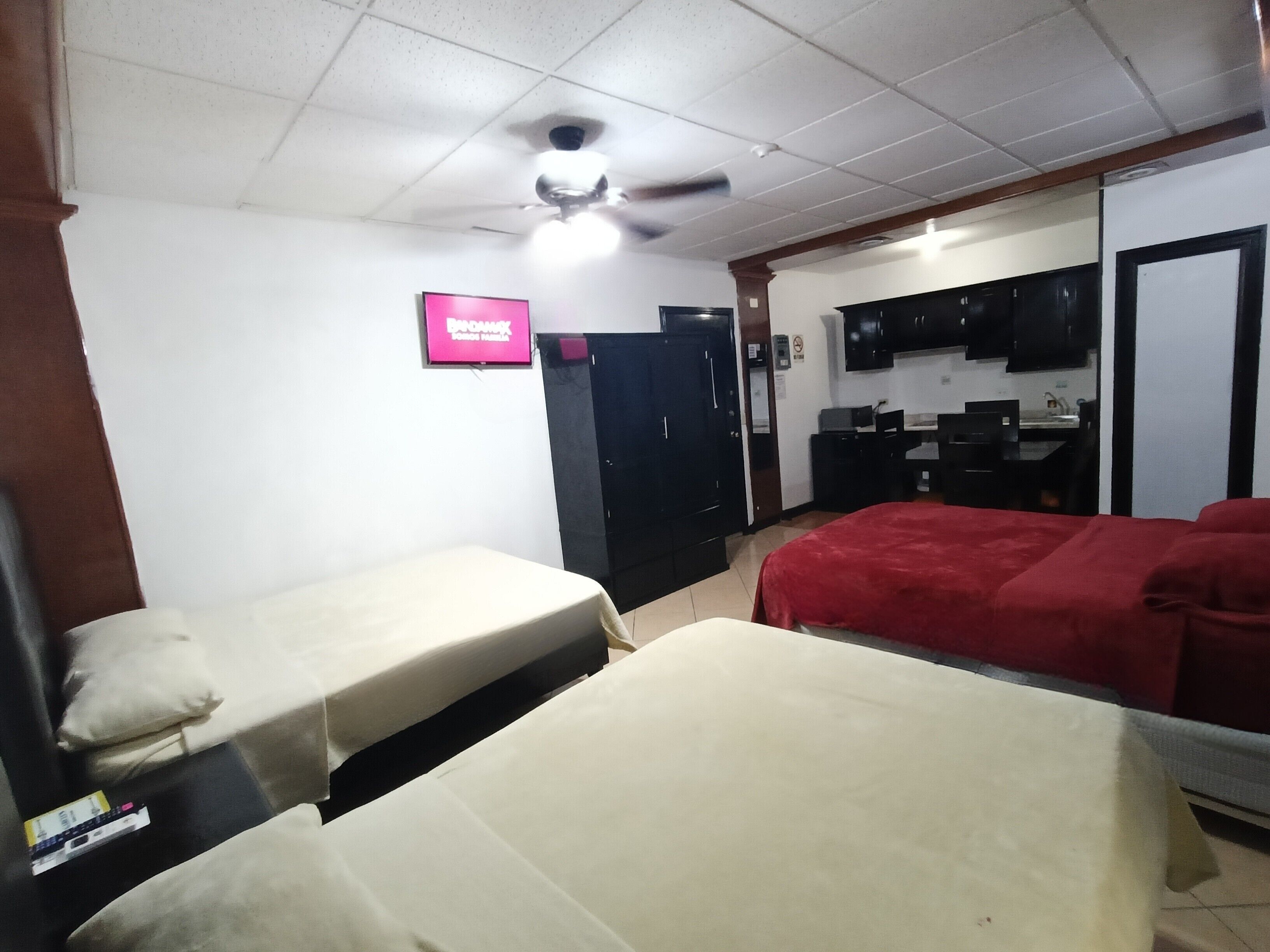 Une chambre d’hôtel avec deux lits, un ventilateur de plafond, une télévision et une kitchenette.